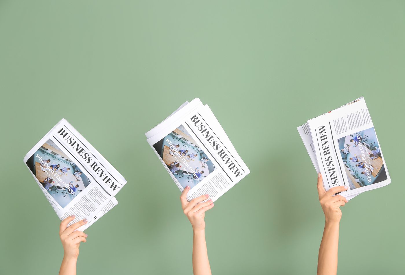 Trois mains brandissent des journaux devant un mur vert